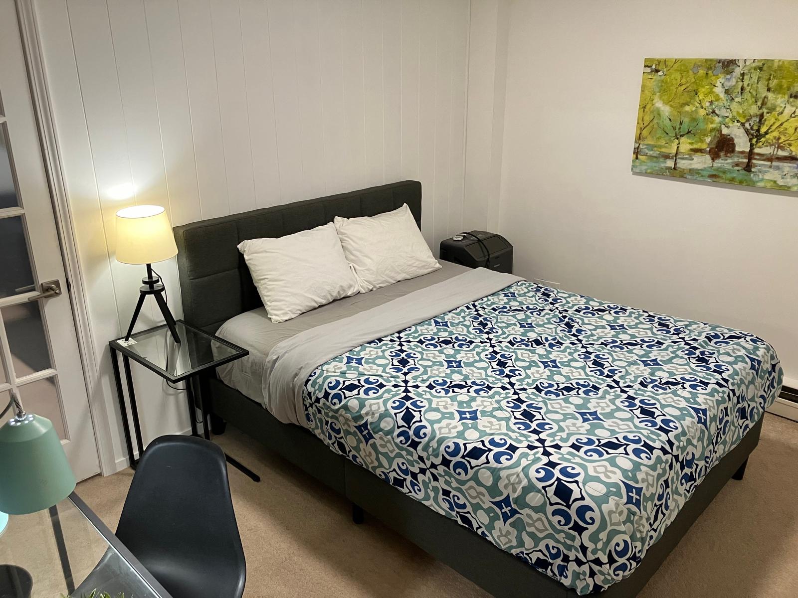 A bedroom with a dark upholstered headboard, white pillows, and a gray comforter.