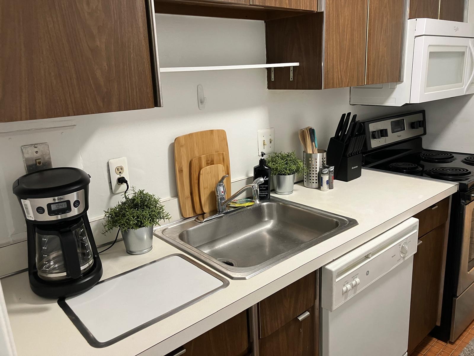A kitchen with dark wood cabinets, a black dishwasher, and a coffee maker beside the sink.