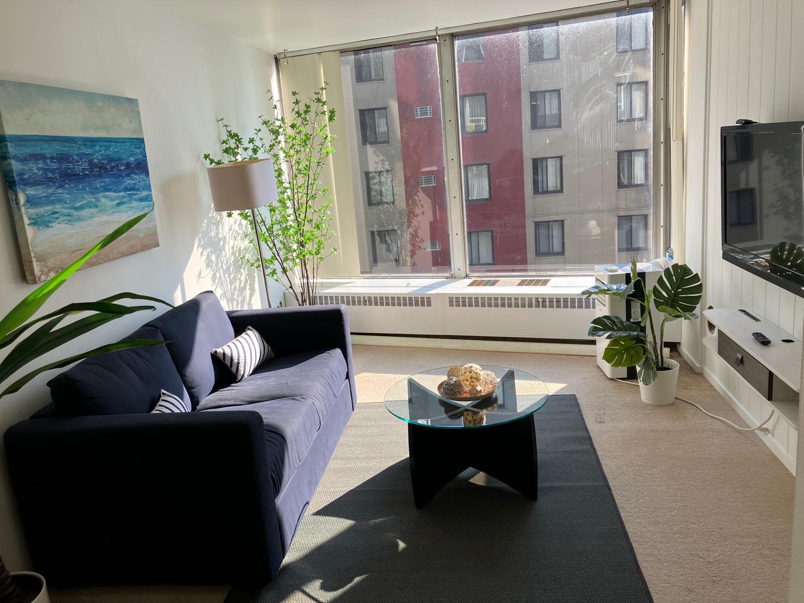 A different Shoreline East living room, with a blue sofa, a glass table, and a wide window.
