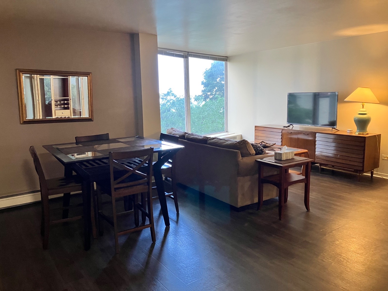 A living and dining room in one Shoreline East condo, with a sofa, a table, and windows onto the trees.